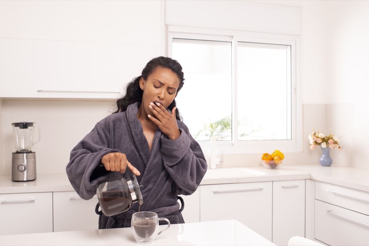 Woman yawning while she pours herself some coffee