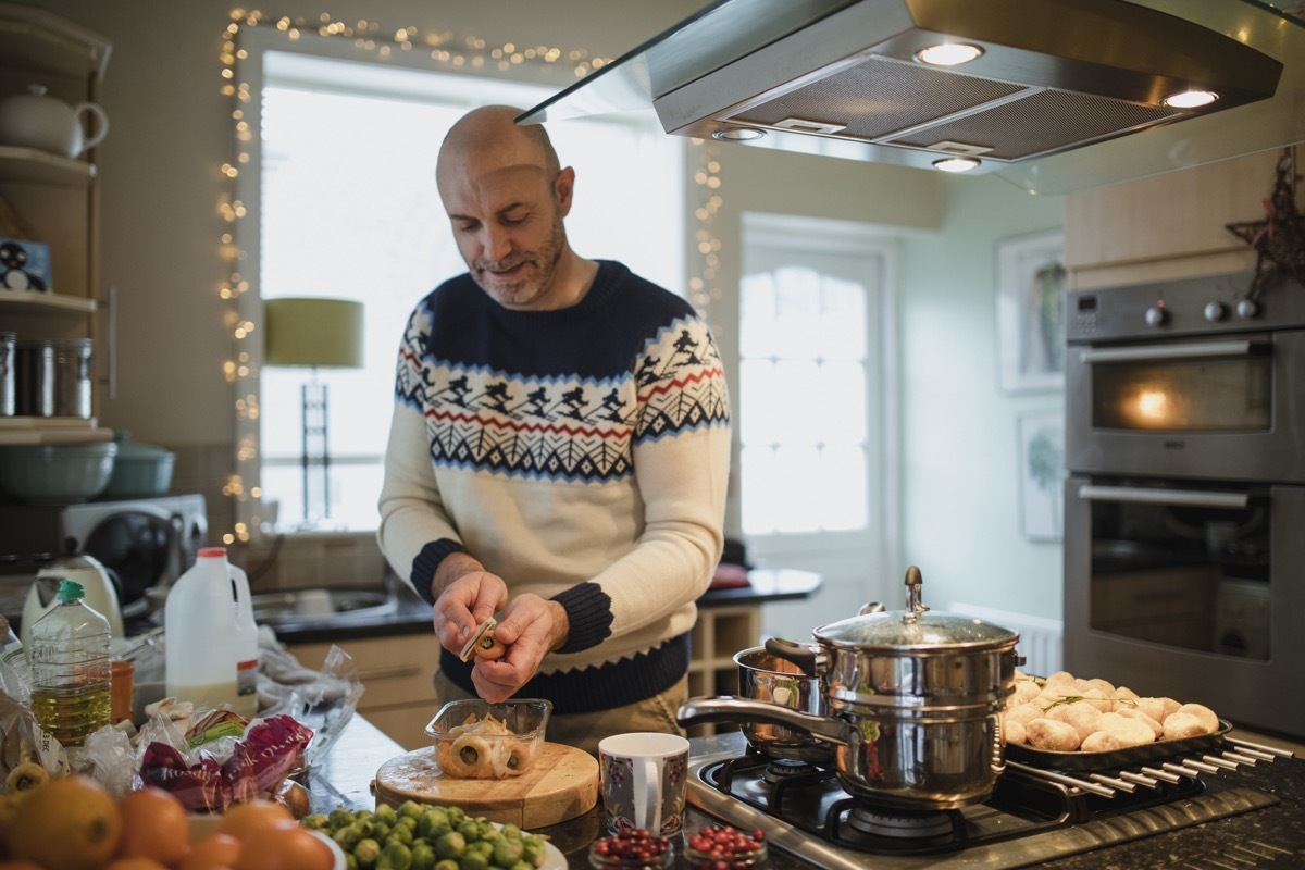 One mature man is preparing a christmas dinner in the kitchen of his home. He is peeling carrots and parsnips.