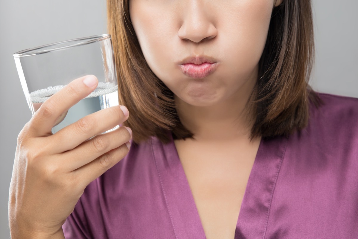 Woman rinsing and gargling while using mouthwash from a glass