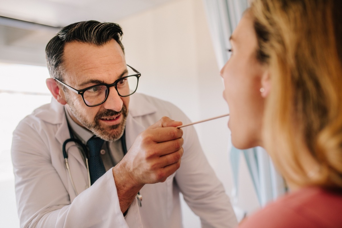 Male doctor checking throat of a female patient with the medical stick. Doctor checking a patients throat.