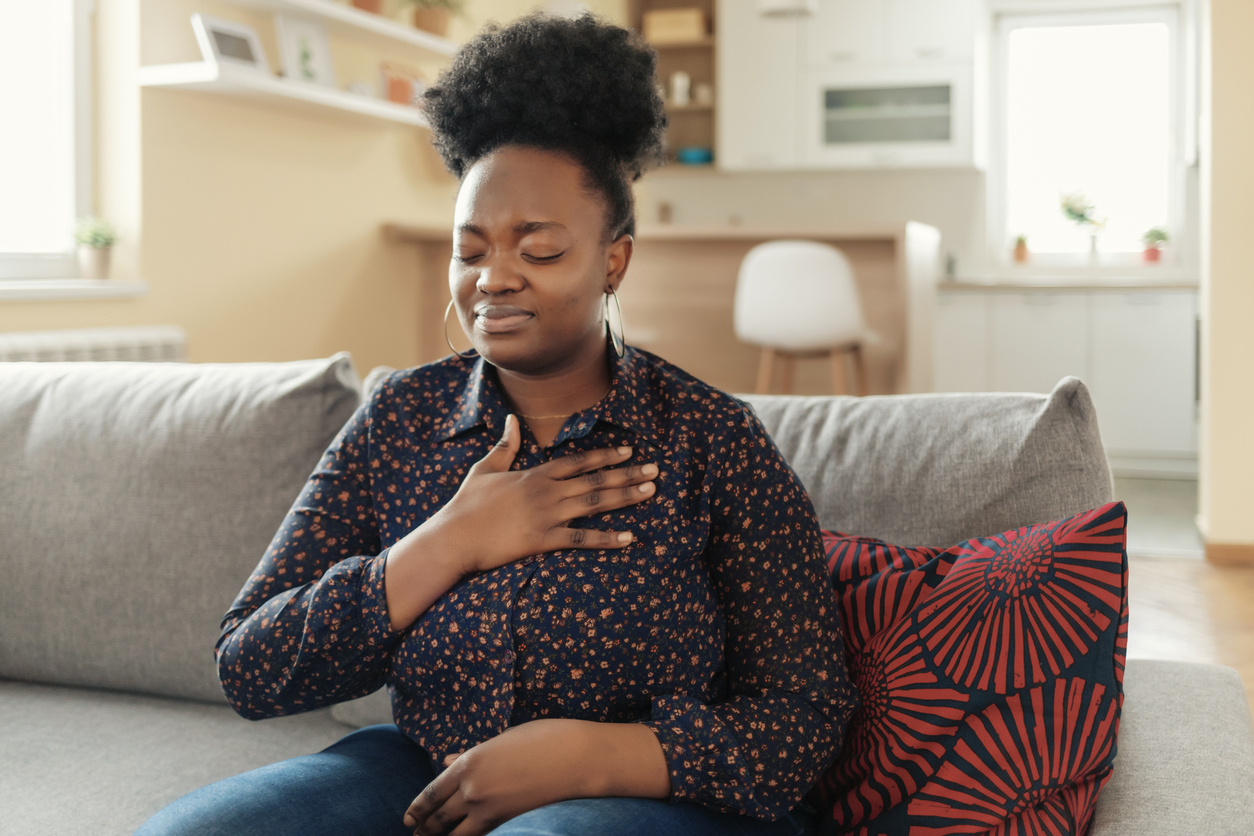 Woman sitting on the couch with her hand on her chest.