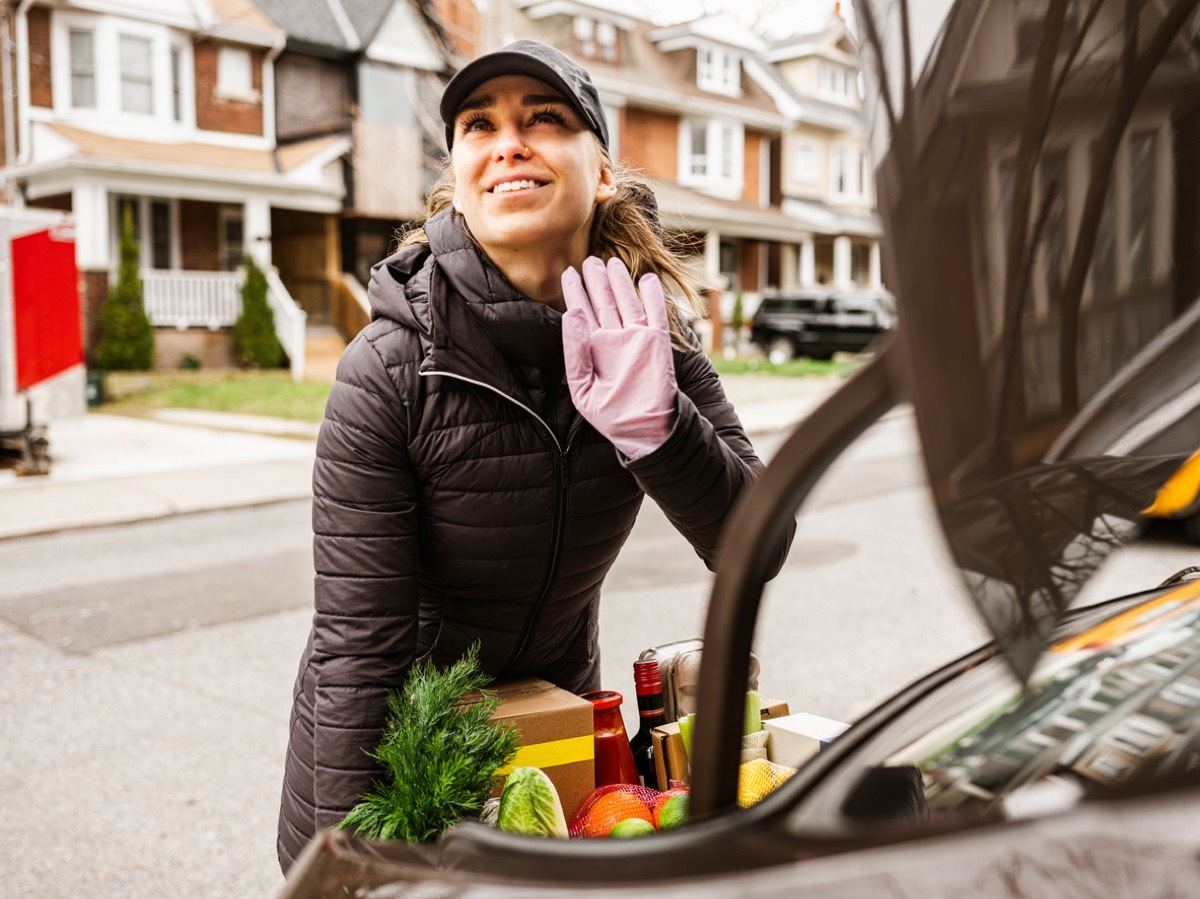 Young woman delivers fresh food during pandemic, waves to someone from afar