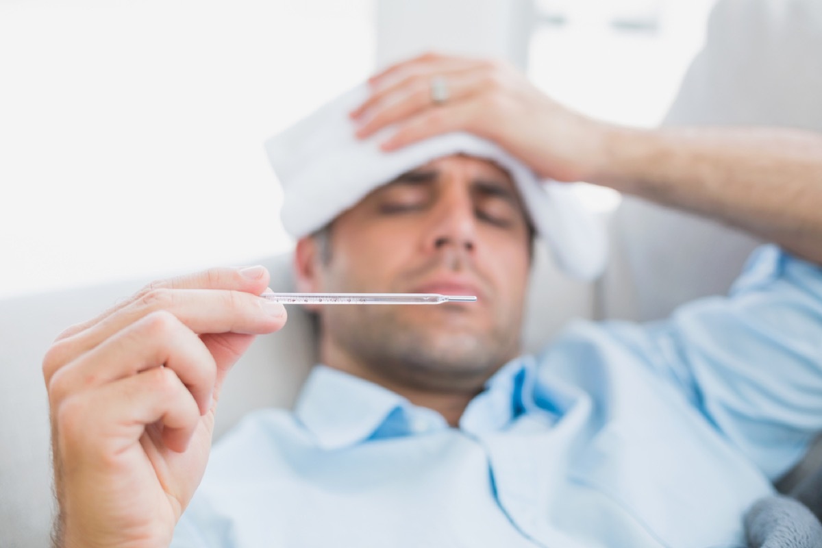 man on couch checking his temperature for fever