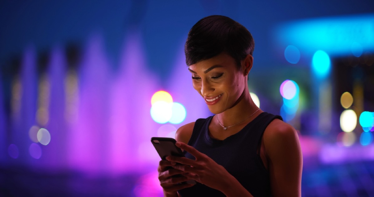 young black woman texting and smiling outside at night