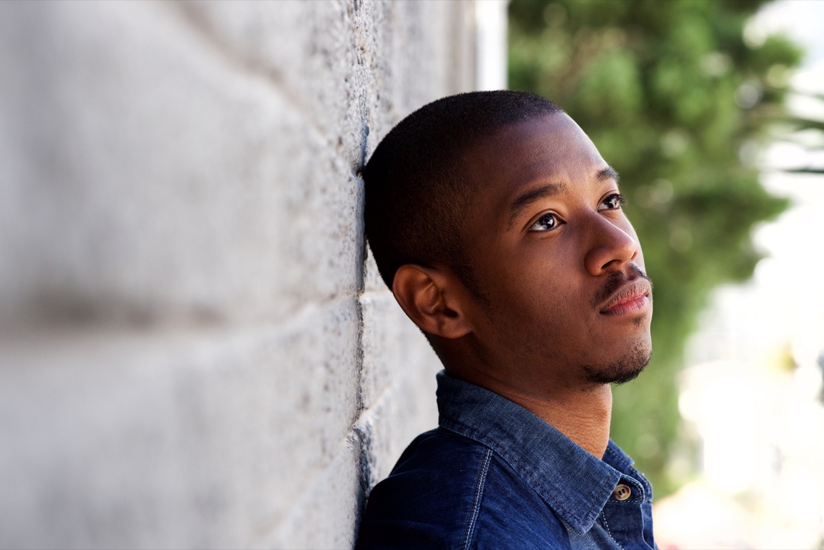 Young black man with shaved head leans against brick wall and stares into distance, things you didn't know had words