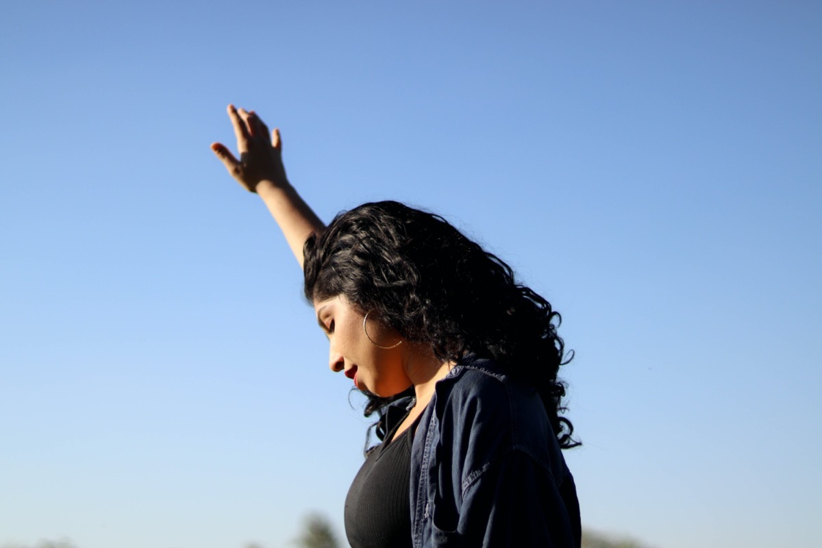 woman holds a hand up to a blue sky