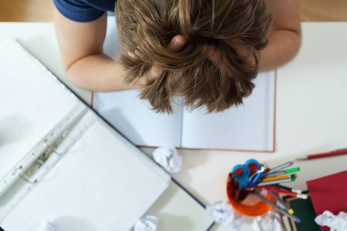 gender neutral person has head in hands while doing homework