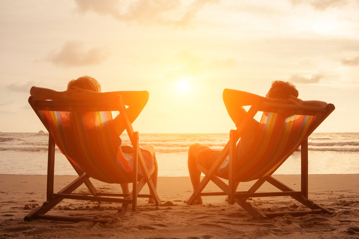 Silhouette of happy young retired couple sitting in deck chairs on the beach at sunset