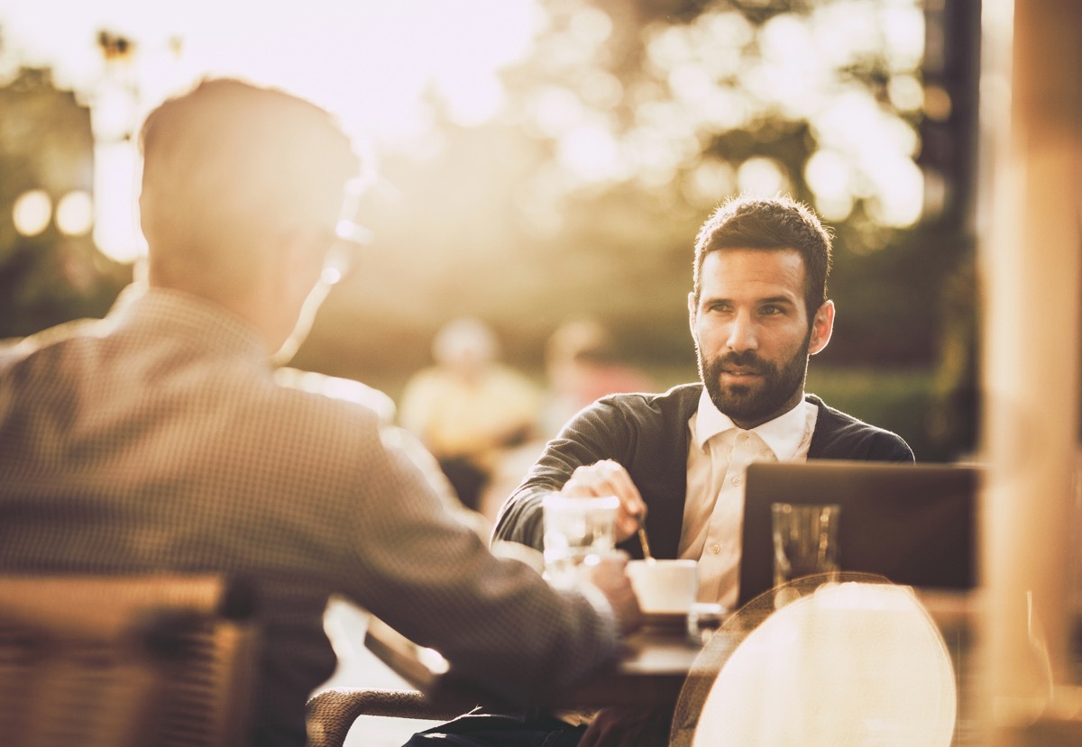 businessman communicating with his colleague while having a coffee break in a street cafe at sunset.