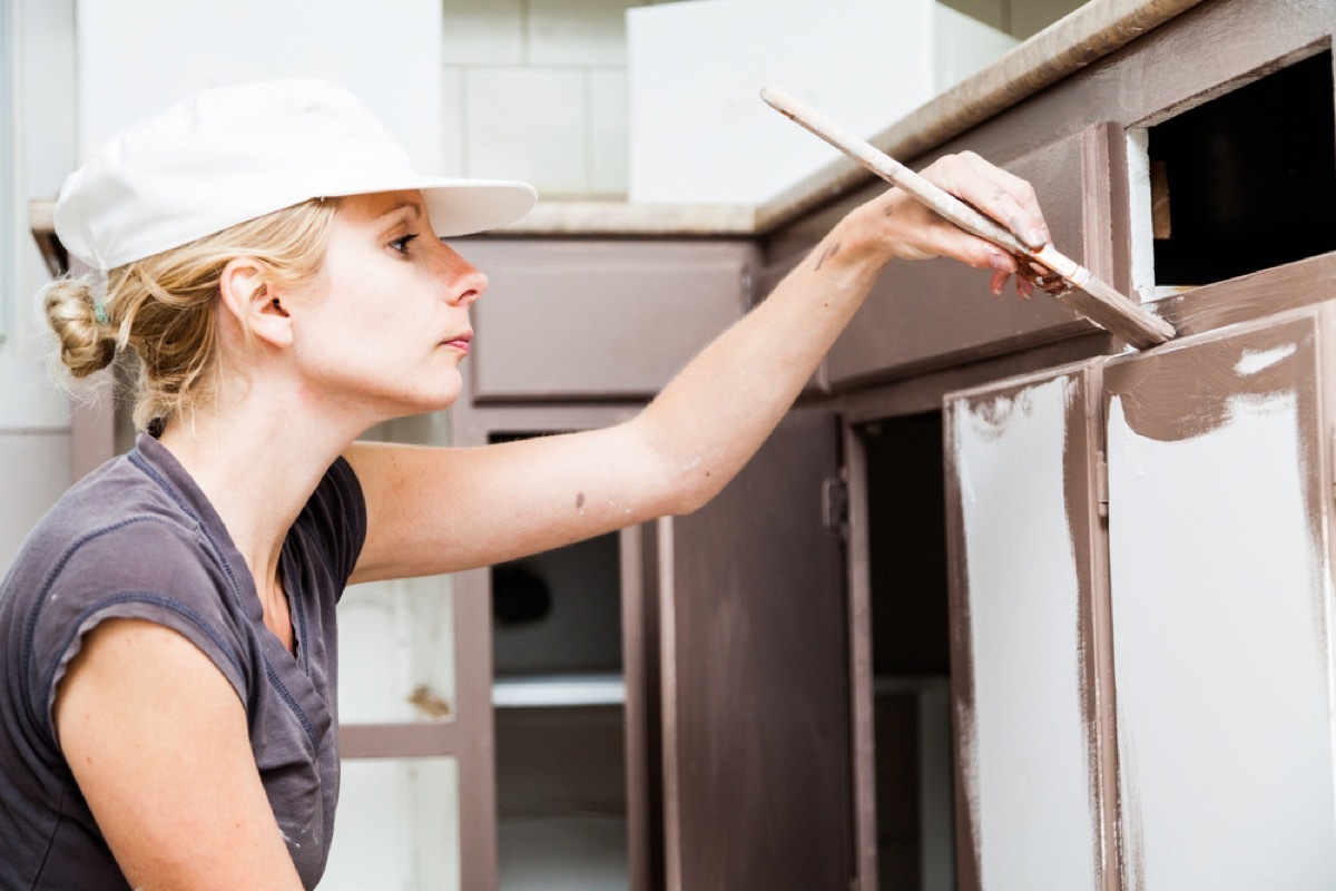 white woman in white hat painting cabinets brown