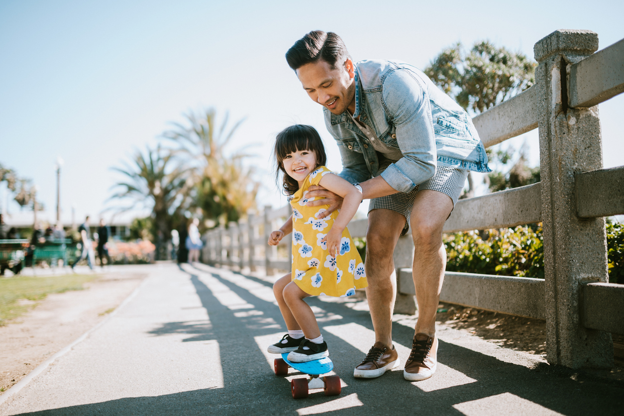 A dad helps his little girl go skateboarding