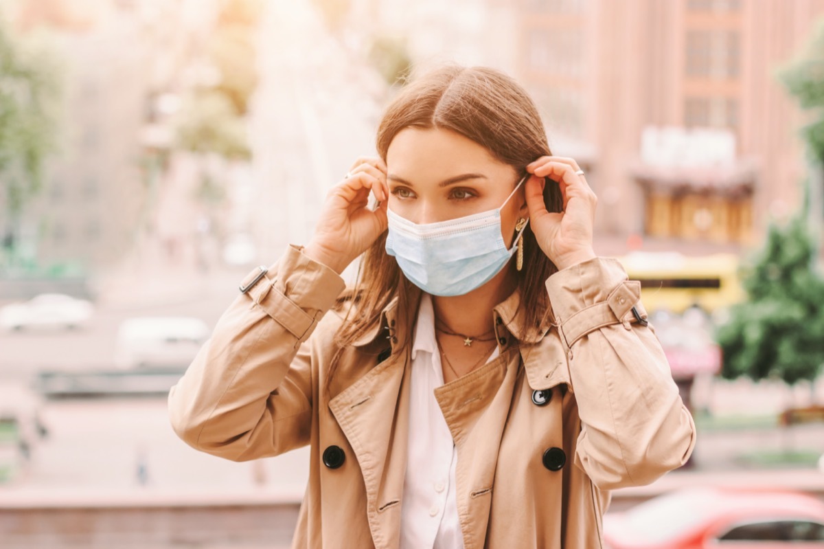 girl wear medical face mask on sunny city street