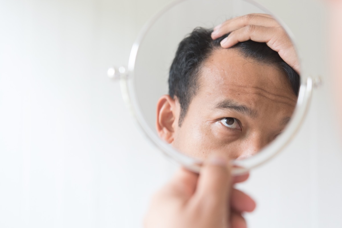 older man looking in mirror at hair loss men's health concerns over 40