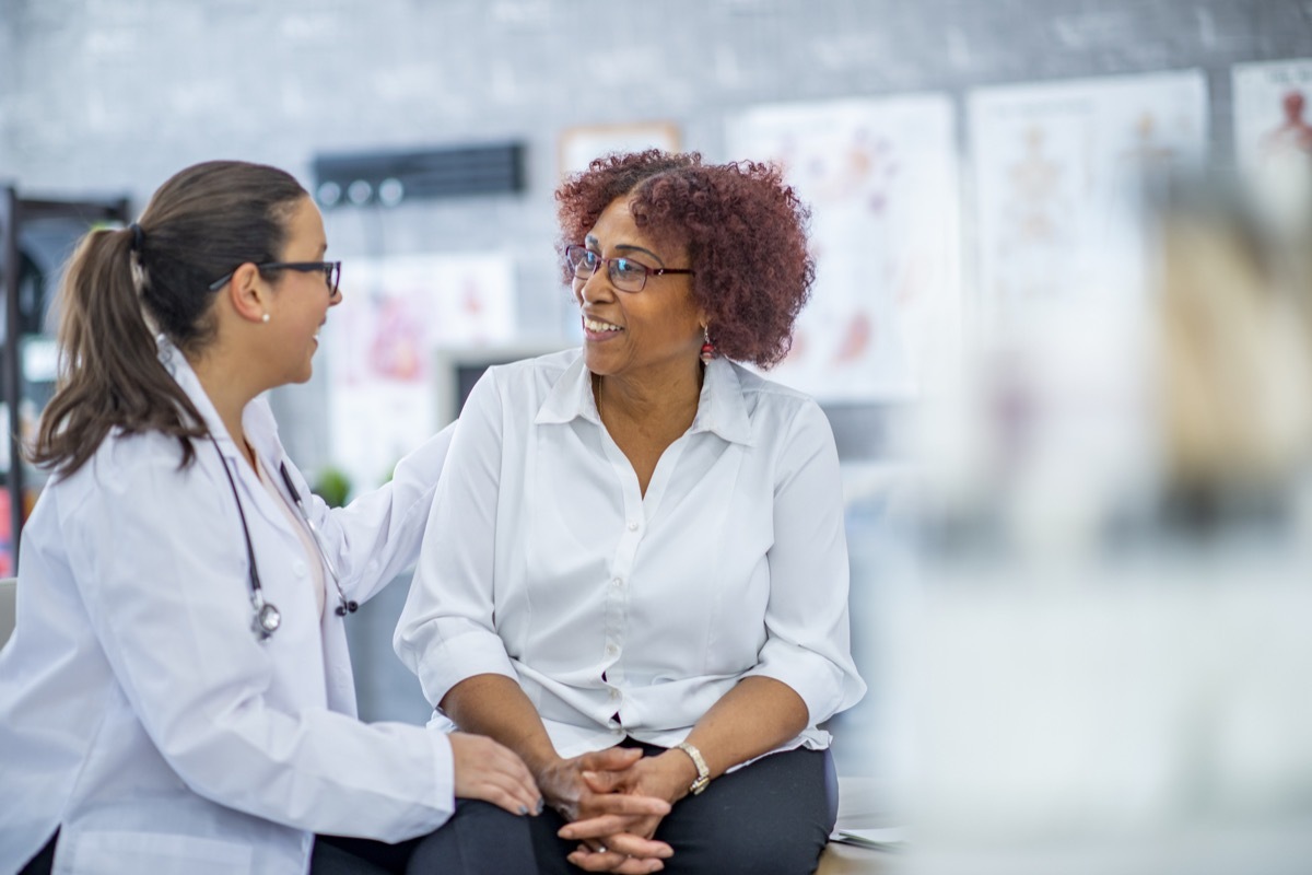 Woman smiles lightly as she discusses with the doctor sitting beside her. They are in a medical office.