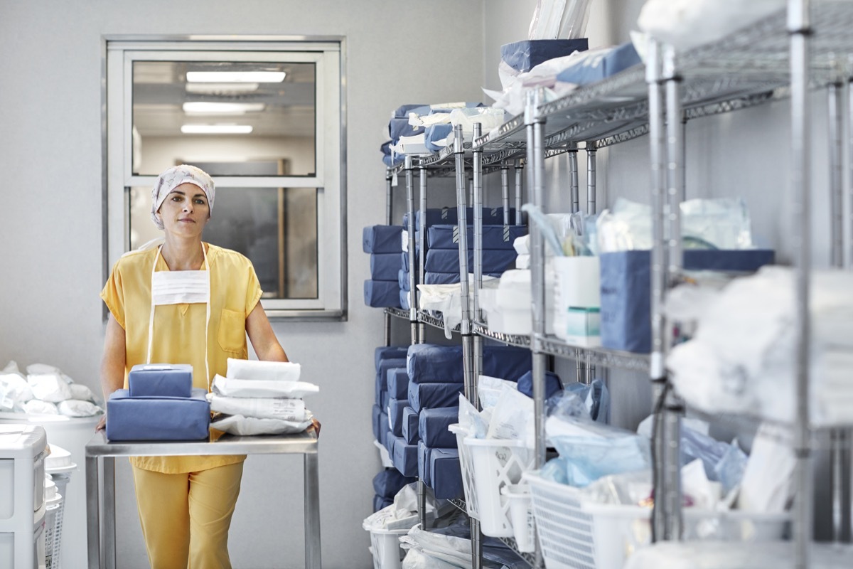 Confident surgeon with medical supplies on trolley. Female healthcare worker is in storage room. She is in hospital.