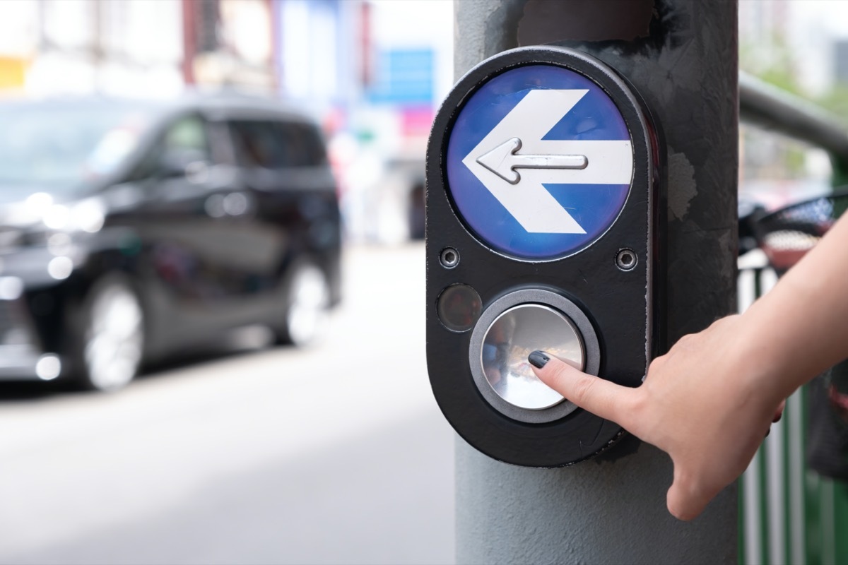 Close up pedestrian crossing call button. Hand pushing button to cross