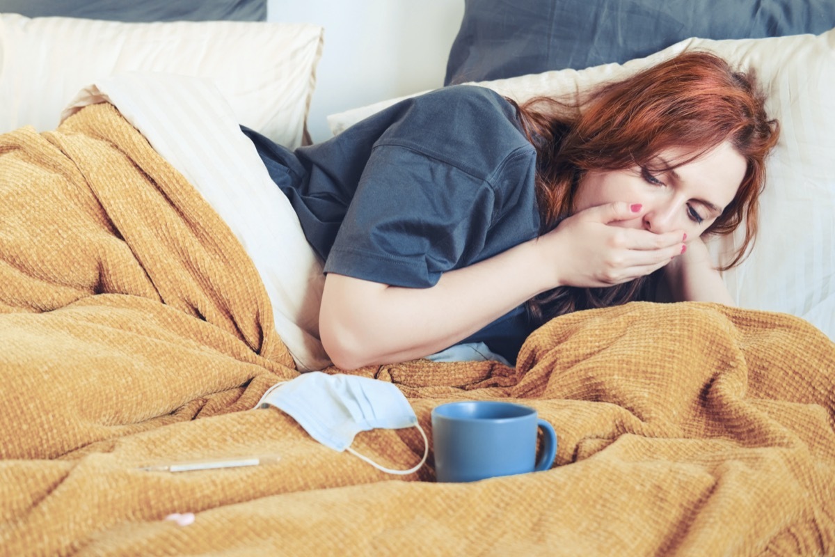 Young woman coughing while lying on bed with a cup of tea