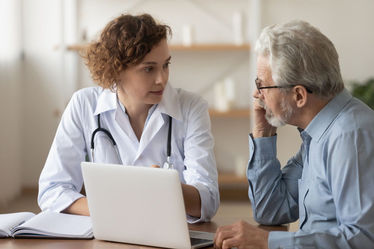 Young professional doctor physician consulting old male patient, talking to senior adult man client at medical checkup visit.