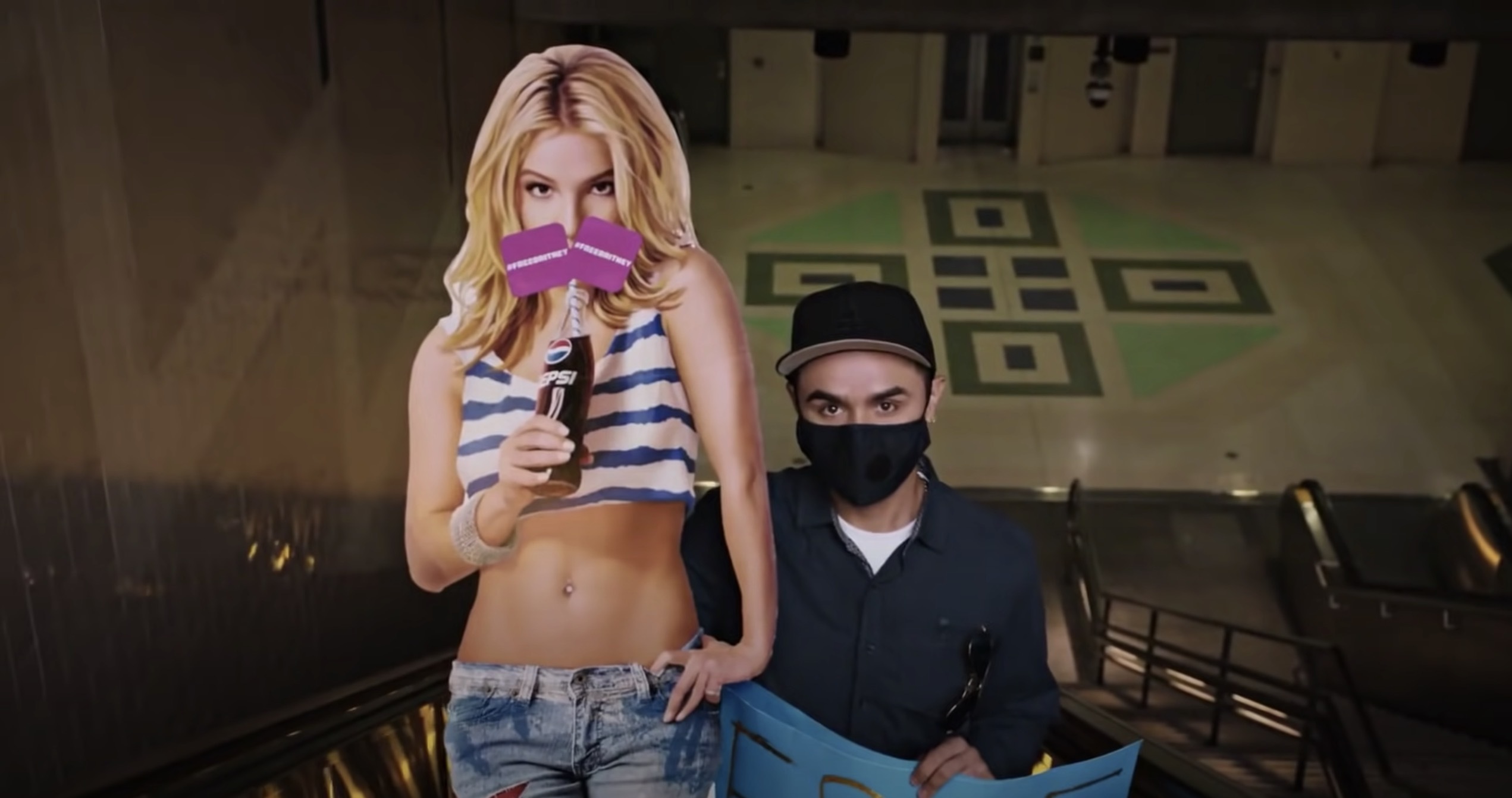 A man wearing a mask sitting next to a cardboard cutout of Britney Spears from the series Framing Britney Spears