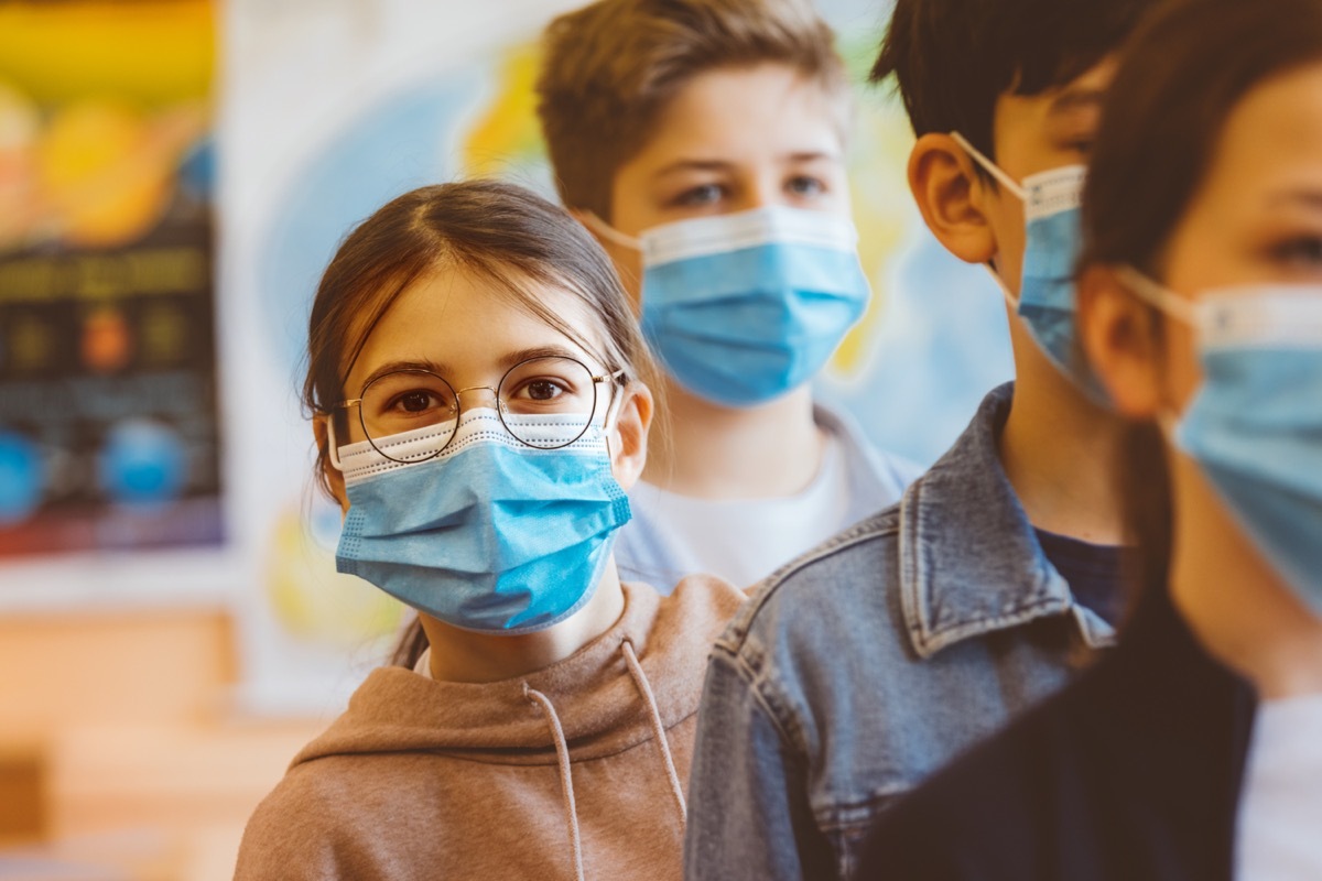 Teenage girl student at a high school standing among the students and looking at camera. All students wearing N95 Face masks waiting in line.