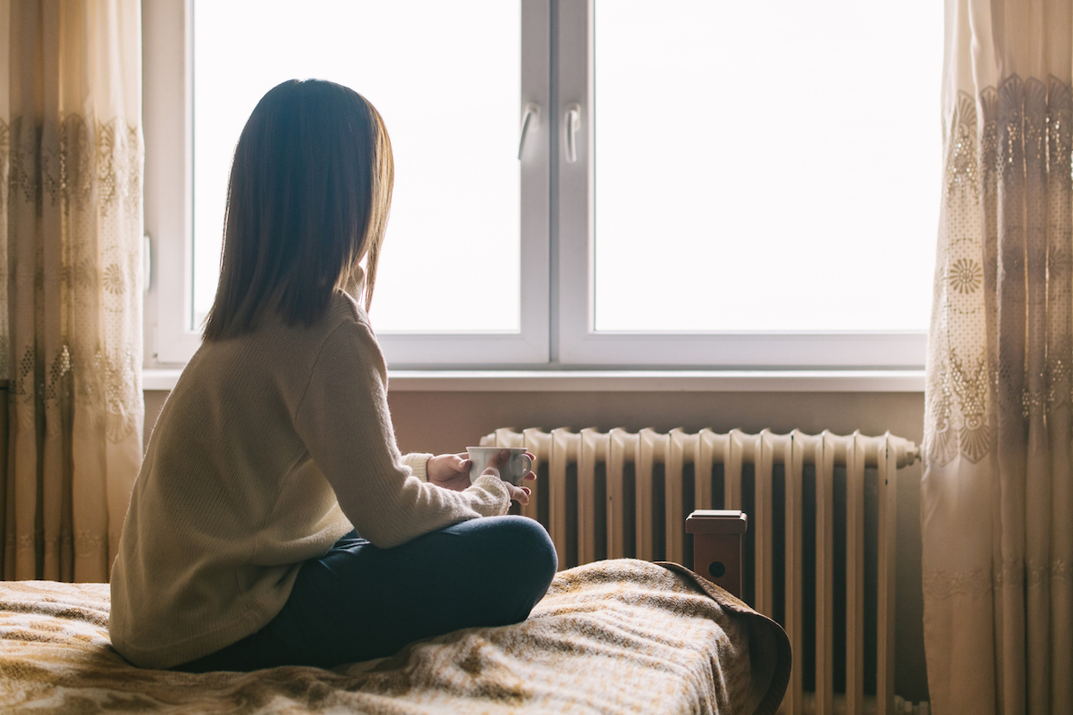 Back view of young woman sitting on bed in the morning