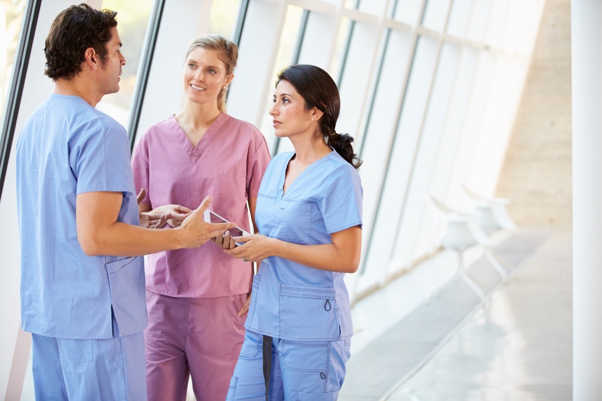 Medical Staff Talking In Hospital Corridor With Digital Tablet