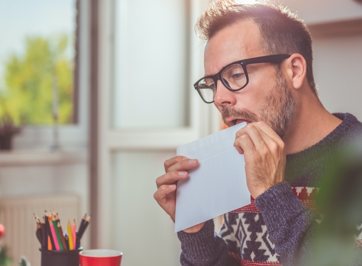 Men wearing blue sweater licking envelope