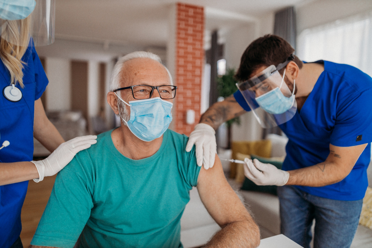 A senior man receives a COVID-19 vaccine booster from healthcare workers