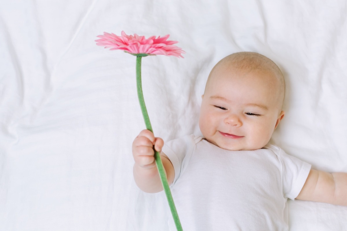 Baby girl holding a flower on her bed