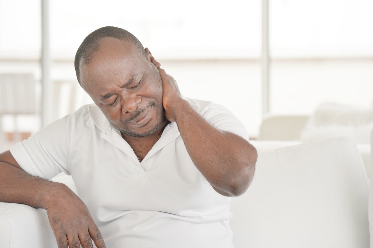 Elderly african man suffering from neck pain at home on couch.