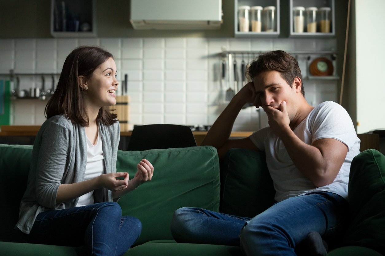 white man yawning while excited white woman talks to him on couch