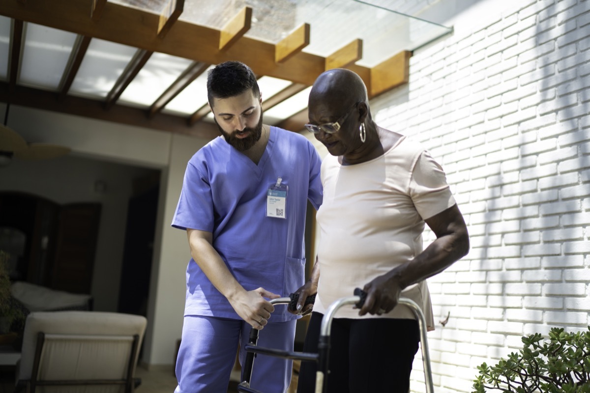 Home caregiver helping senior woman to walk