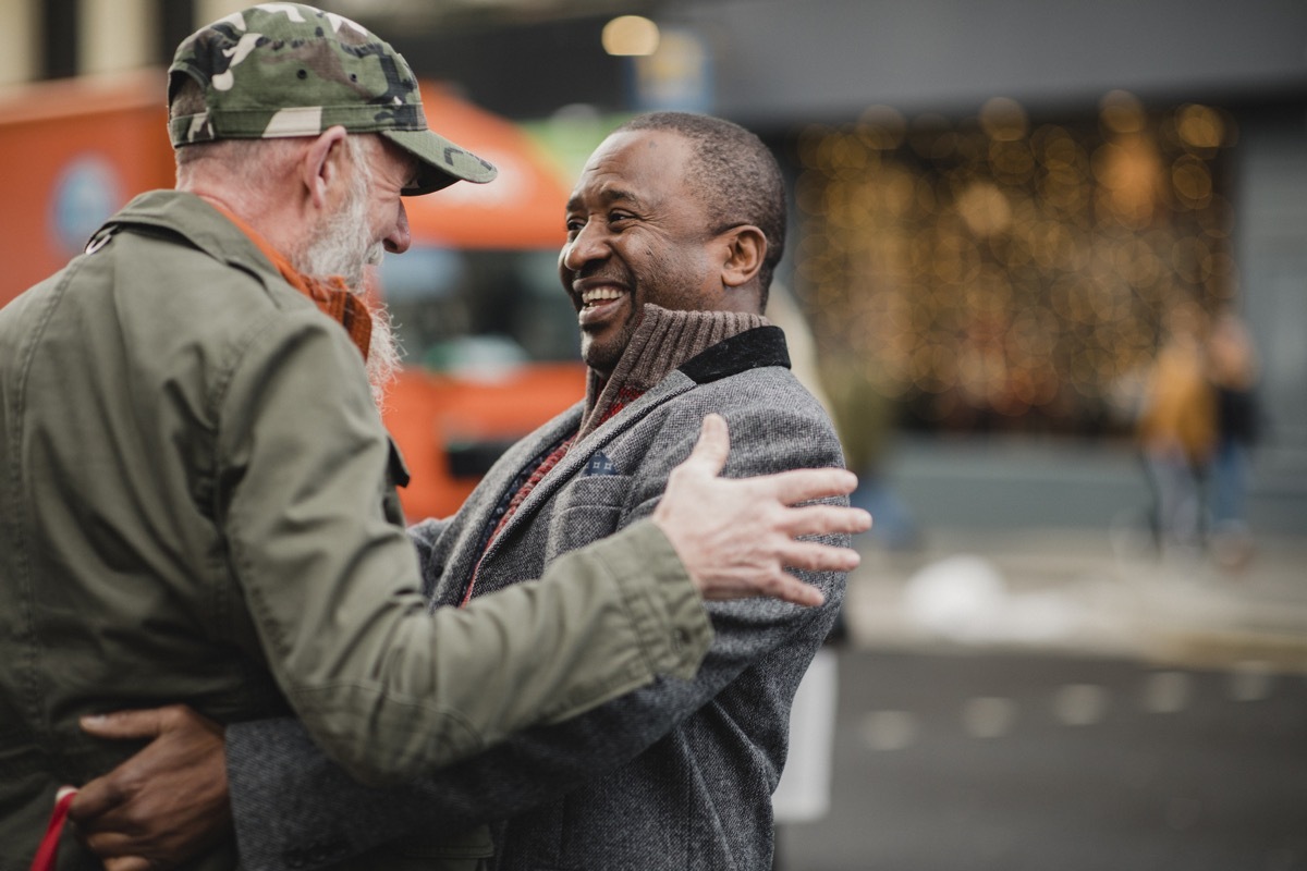 Two senior men have bumped into each other in the city and are greeting each other with a friendly hug.