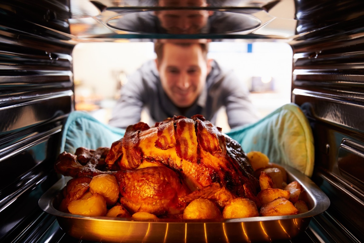 Young white man taking turkey out of oven