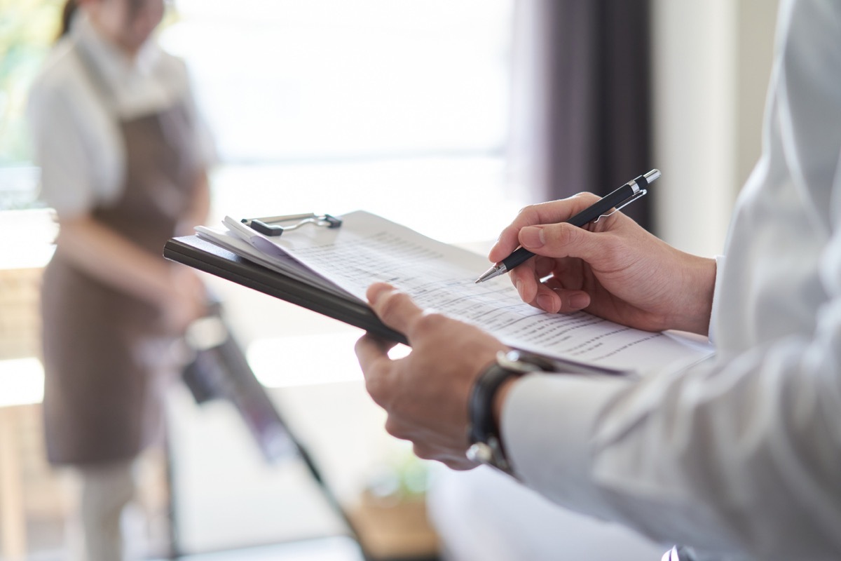 man checking off maid requirements on paper as she cleans