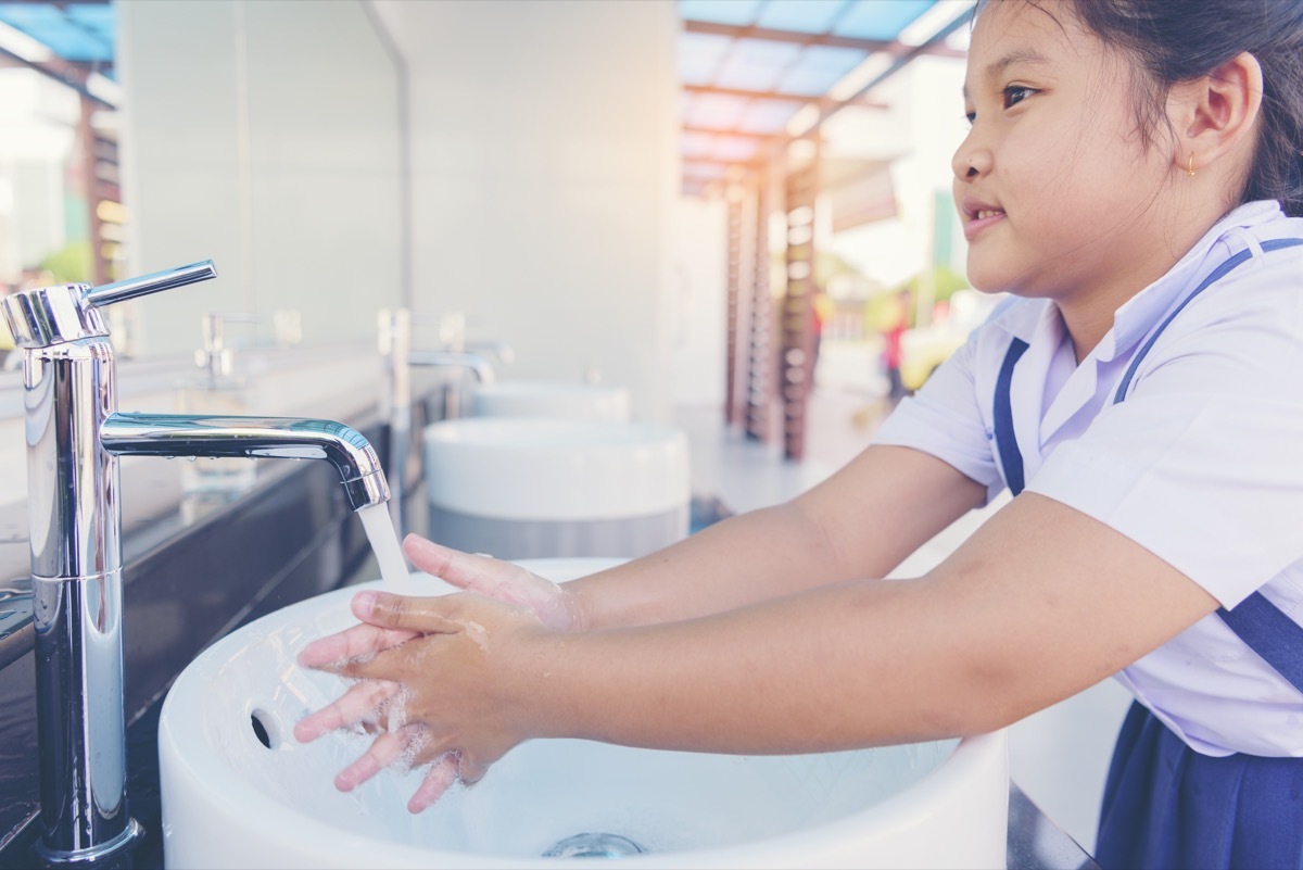 A little girl washing her hands in a school bathroom classroom surfaces germs