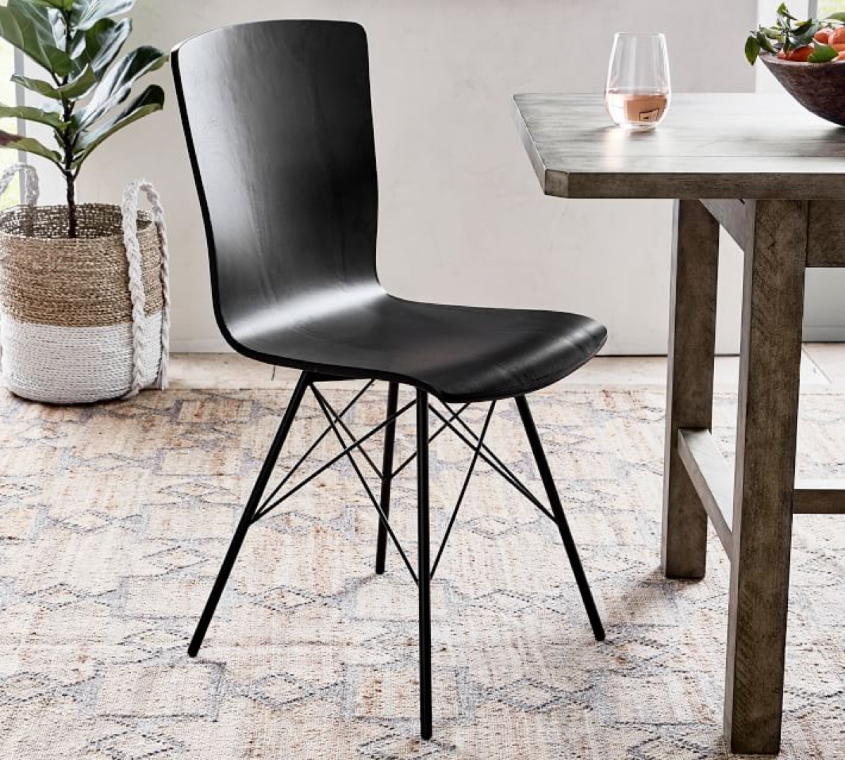 black dining room chair next to wooden table and plant in two-toned pot