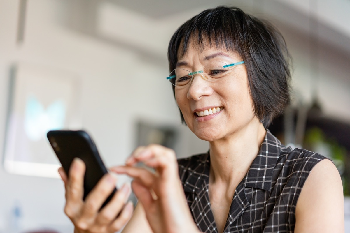 Senior Asian woman laughing when using a smartphone.