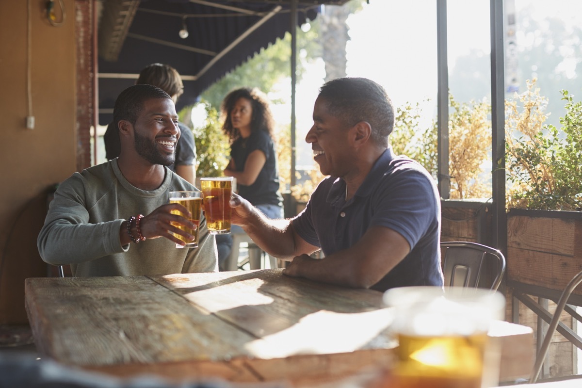 two middle aged black man toasting beer on the patio at a sports bar