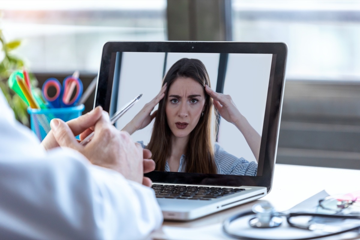 Back view of a doctor attending to a woman patient through a video call with the laptop at home.