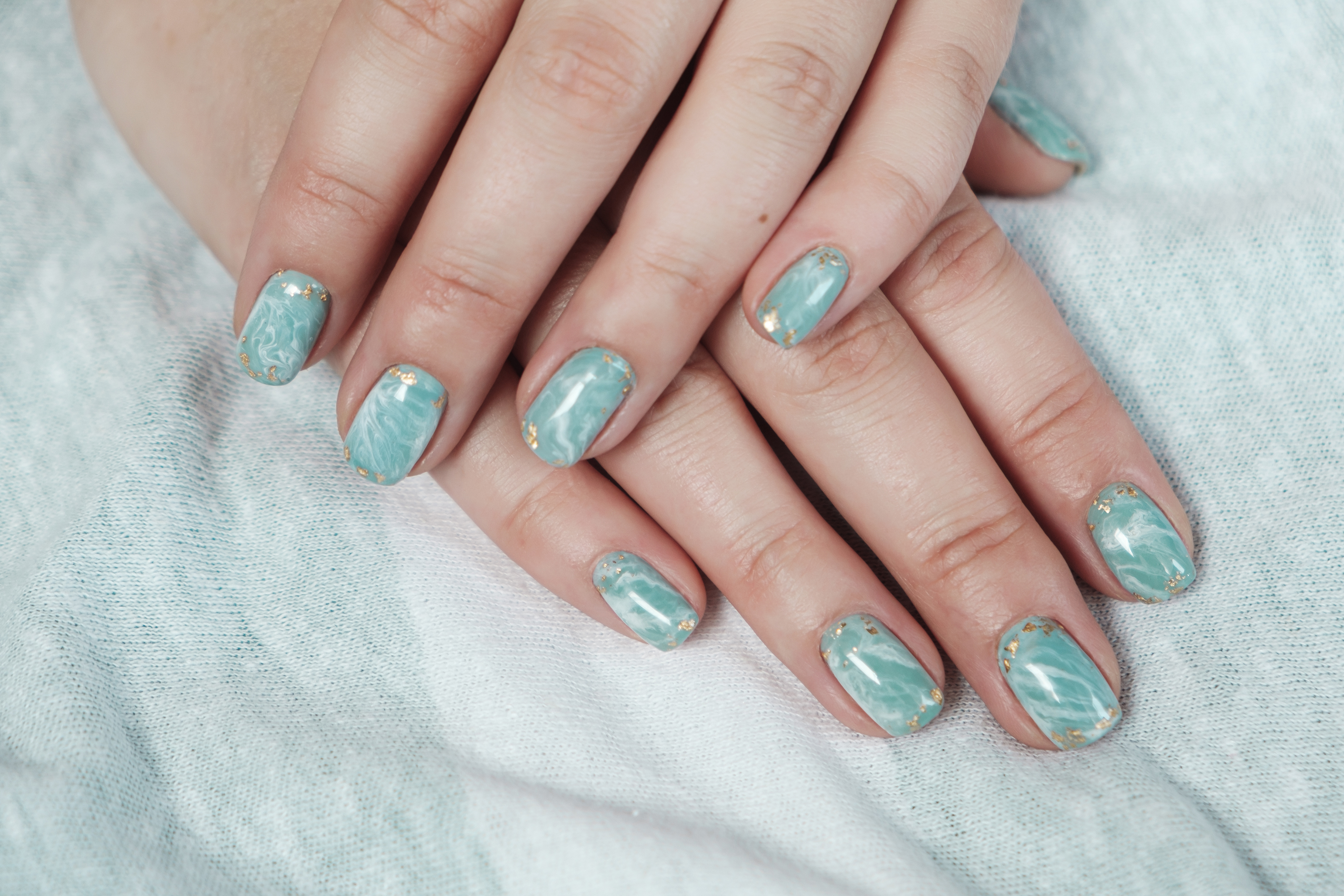 Model woman hand showing shellac marble green pastel manicure with gold leaf on short nails