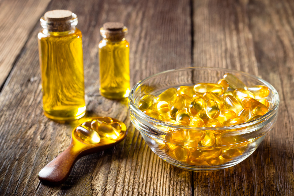 Omega-3 fish oil capsules in a bowl and vials on a wooden table