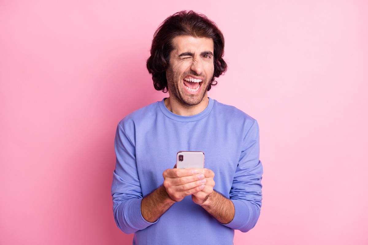 man on his phone winking over pink background