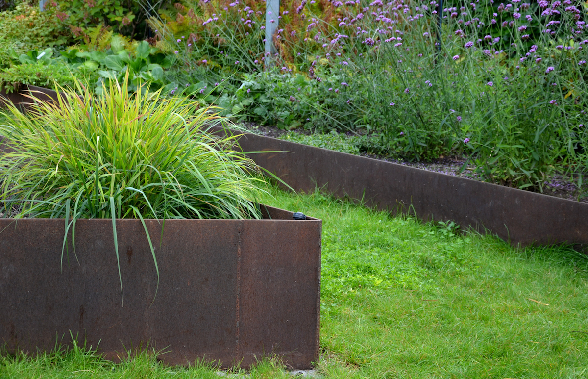 brown flower pots in the garden, park filled with water. the surface of the flowerpot is intentionally rusty in design. inside are ornamental aquatic plants. around is a limestone paving with large joints