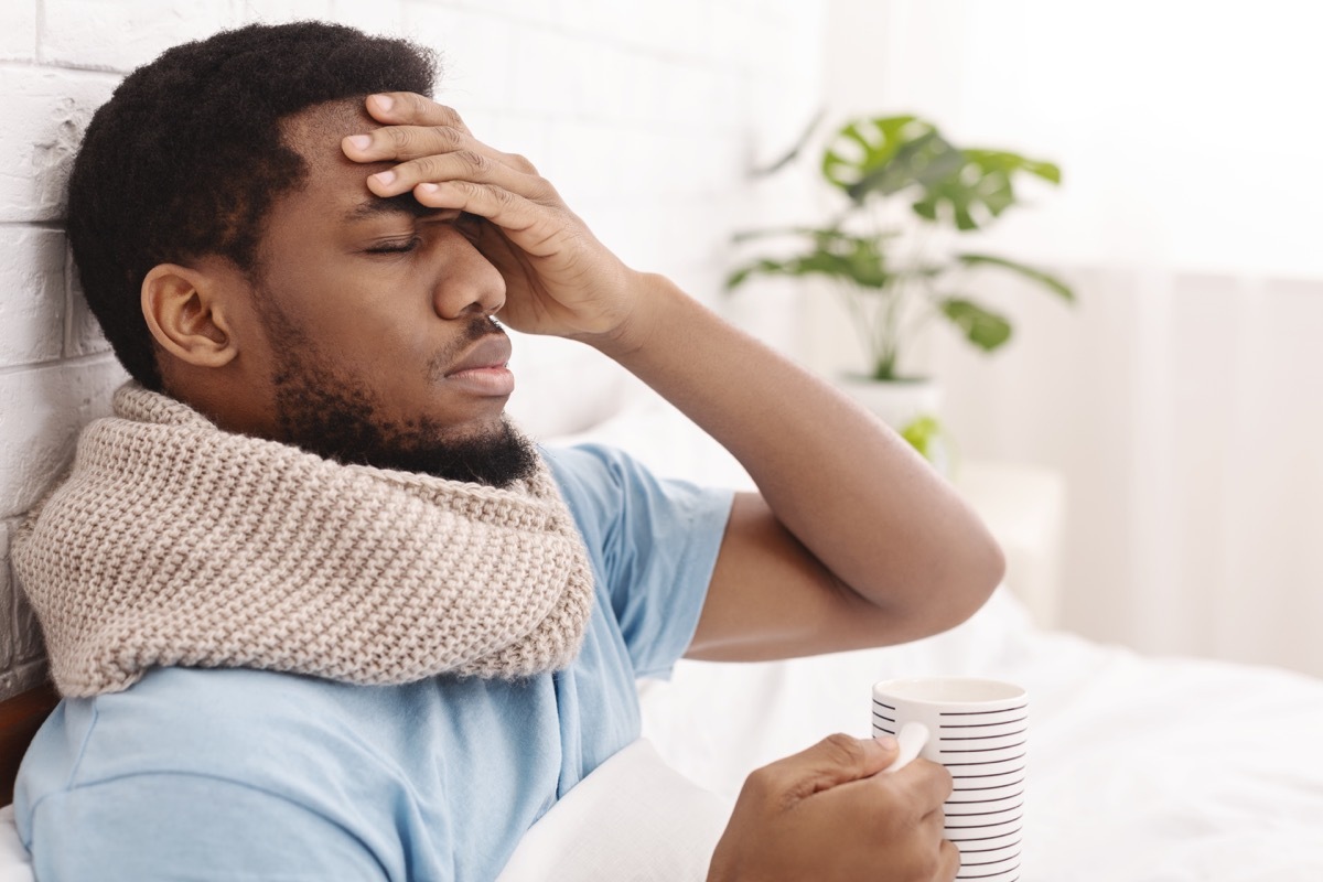 Sick man having fever, drinking hot healing tea and touching forehead in bed,