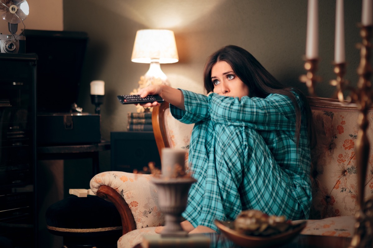 Sullen woman watching television on her couch in pajamas