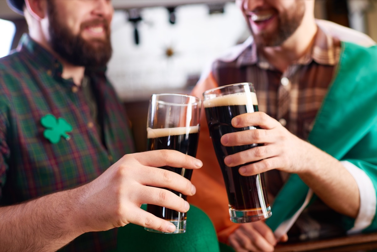 cheerful men in costume clinking beer glasses while celebrating St Patrick day