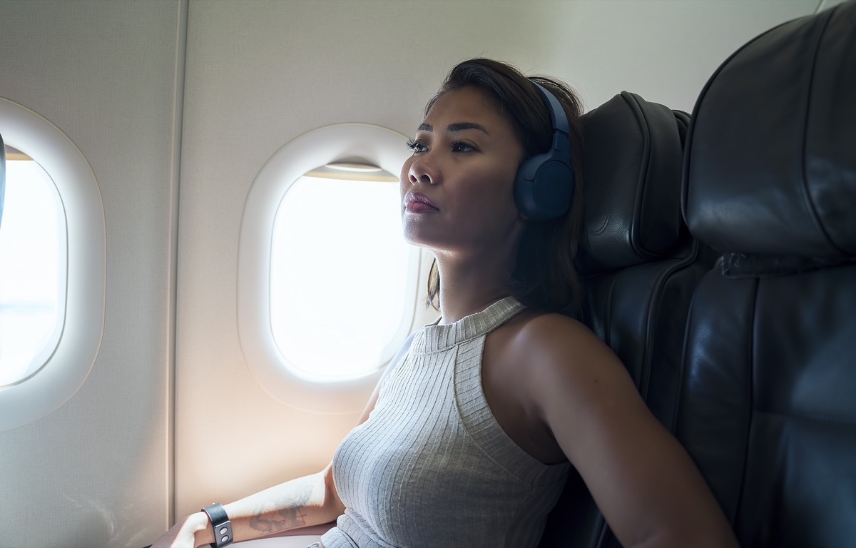 Woman wearing headphones sitting in window airplane seat