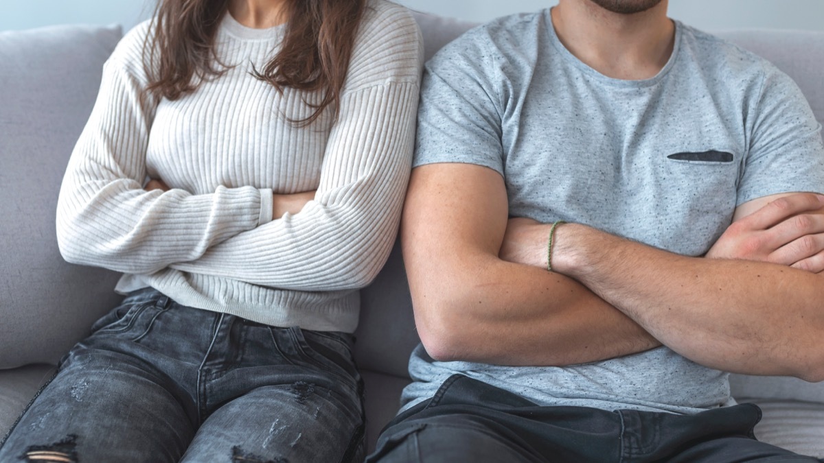 Young white couple, closeup of arms folded on couch, body language cues from wife to husband