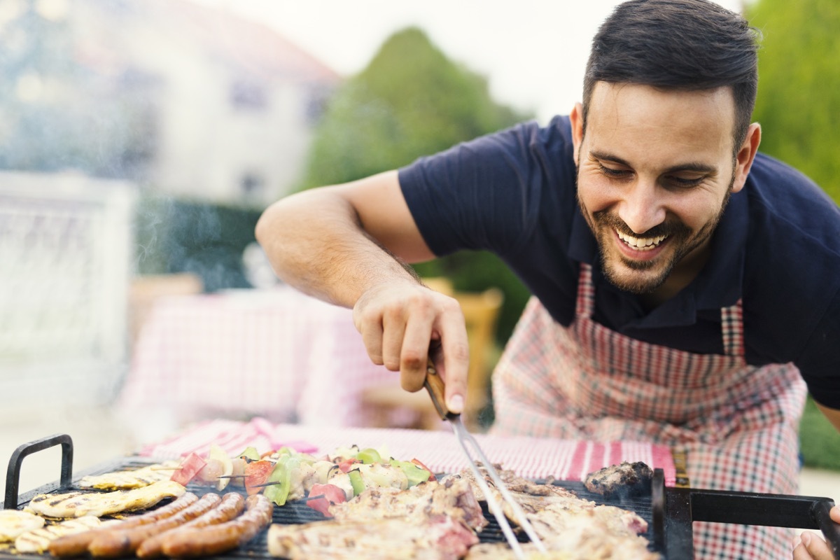 30-something man checking meat on the grill